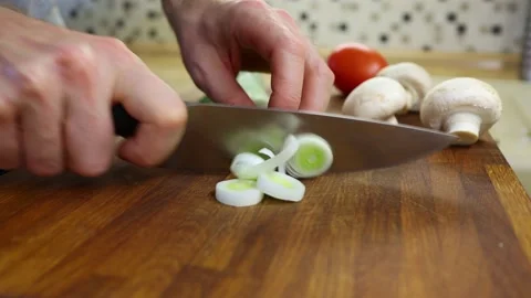 The chef slices leeks on an oak board. Tomato and mushrooms on the background Stock Footage 156692715