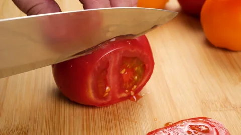 A chef slices a ripe red tomato on a wooden cutting board with a sharp knife. Video stock 341546980