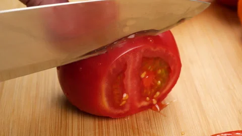 A chef slices a ripe red tomato on a wooden cutting board with a sharp knife.  Stock Footage 342285868