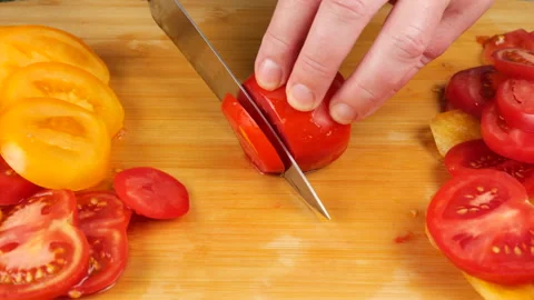 A chef slices ripe red tomatoes on a wooden cutting board with a sharp knife. Stock Footage 341548018