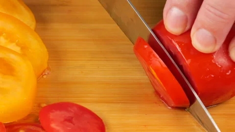 A chef slices ripe red tomatoes on a wooden cutting board with a sharp knife. Stock Footage 342285822