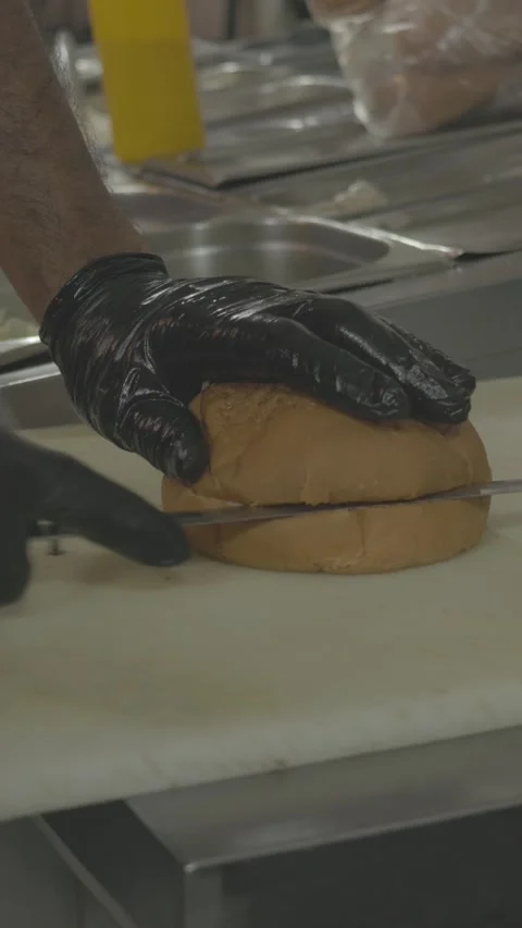 Chef slicing burger bun with knife, gloved hands on bread Stock Footage 305795450