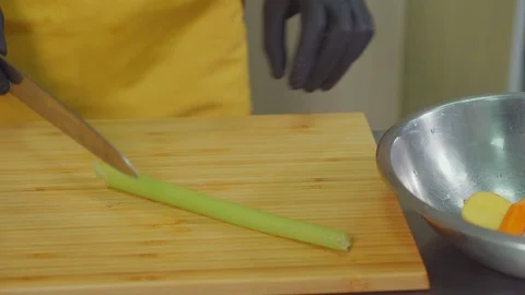 Chef is slicing celery stalk on cutting board in kitchen and putting it in bowl Stock Footage 102975285