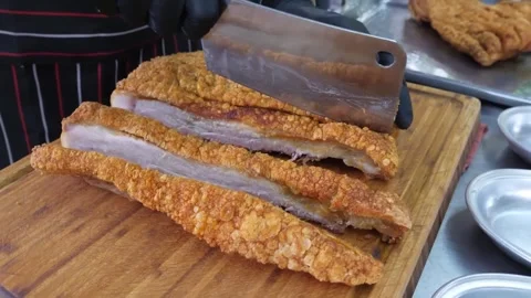 Chef Slicing Crispy Roasted Pork Belly with Golden Crackling Skin on Wooden Boar Stock Footage 338211872