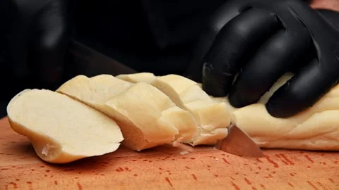 Chef slicing fresh bread on wooden cutting board with black gloves visible Stock Footage 336678045