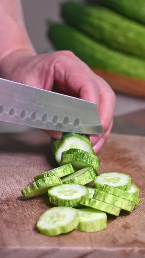 Chef slicing a fresh green cucumber with a knife on a wooden cutting board Stock Footage 336160127