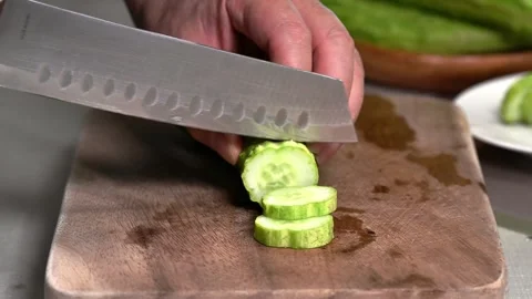Chef slicing a fresh green cucumber with a knife on a wooden cutting board Stock Footage 336160129