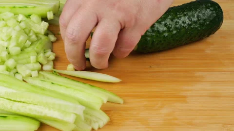 A chef is slicing a fresh green cucumber with a sharp knife on a cutting board. Stock Footage 342285720