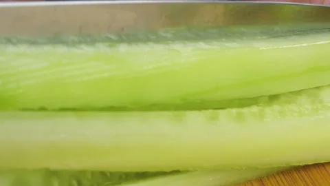 A chef is slicing a fresh green cucumber into long strips on a cutting board. Stock-Footage 342286603