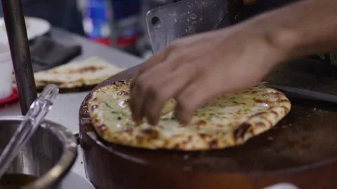 Chef Slicing Fresh Naan Flatbread on Wooden Board With Cleaver Stock Footage 345714975