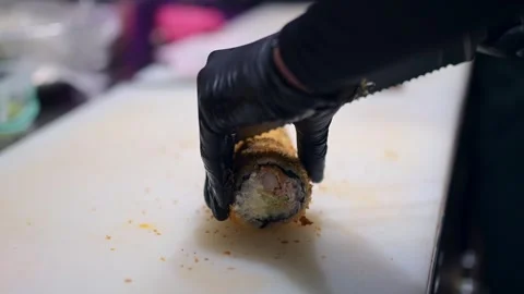 Chef slicing a fried sushi roll with a serrated knife, black gloved hand holding Stock Footage 293486723