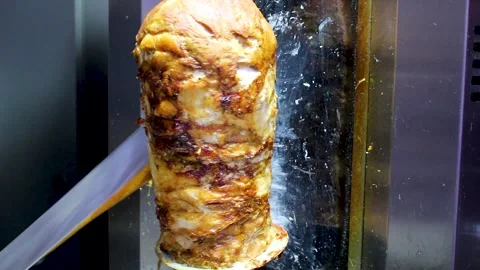 Chef slicing juicy roasted meat from a vertical rotisserie spit Stock Footage 345615771