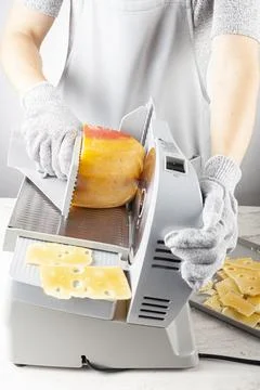 A chef is slicing a large chunk of swiss cheese using an electrical deli slic Stock Photos