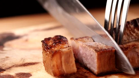 Chef slicing medium or well done beef steak with knife and fork Stock Footage 222779708