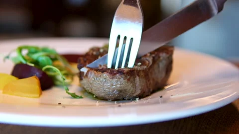 Chef slicing medium or well done beef steak with knife and fork on wooden Stock Footage 291989366