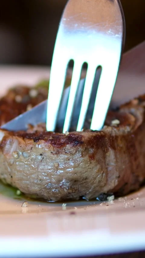 Chef slicing medium or well done beef steak with knife and fork on wooden Stock Footage 292452447