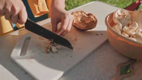 Chef slicing mushrooms on camping kitchen setup with sunlight. Outdoor camping Stock Footage 337826415