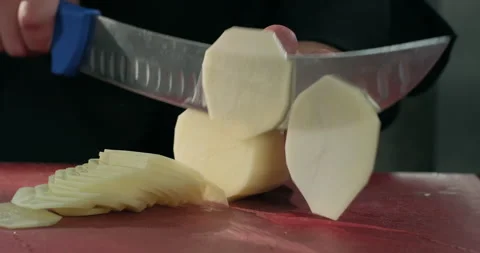Chef slicing potato with a big knife on a cutting board, preparing a meal. Close Stock Footage 294225972