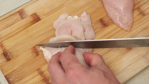 Chef slicing raw chicken breast on cutting board for cooking tutorial Stock Footage 317579227
