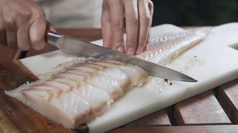 Chef is slicing raw codfish on the board before roasting it, cooking outdoors Stock Footage 77579520