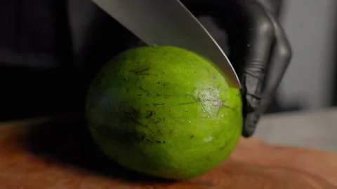 Chef slicing ripe avocado in half on wooden board with sharp knife Stock Footage 313028904