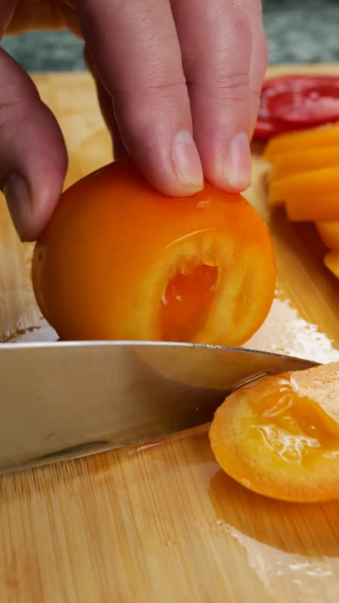 Chef slicing a ripe orange tomato on a wooden cutting board. 스톡 동영상 341472368