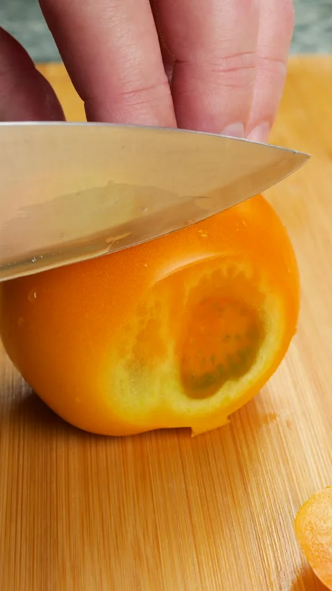 Chef slicing a ripe orange tomato on a wooden cutting board. 스톡 동영상 342280192