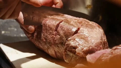 Chef slicing roasted meat into thick portions on board Stock Footage 345930320
