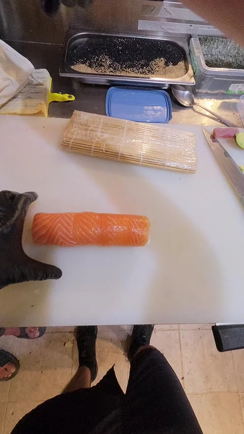 Chef slicing salmon sushi roll with a sharp knife on a cutting board Stock Footage 314498664