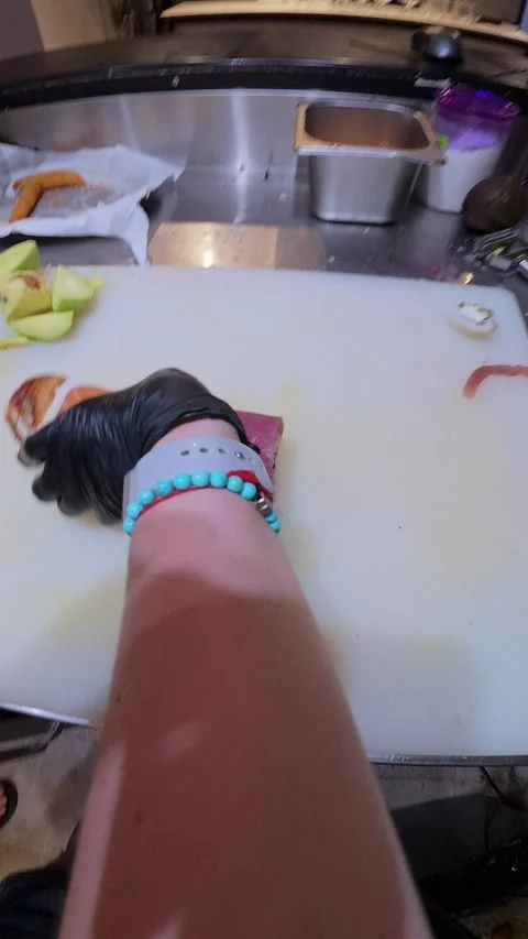 Chef slicing sushi roll with avocado and salmon topping on cutting board in Stock Footage 314497283
