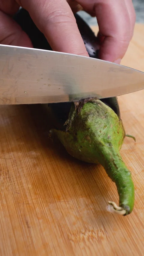 Chef slicing off the top green stem of a fresh eggplant on a cutting board. Video stock 341533974