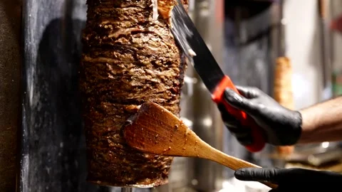 Chef slicing vertical shawarma spit with sharp knife, juicy layers of grilled   Stock Footage 313880467