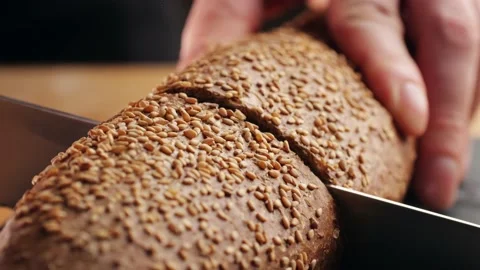 Chef slicing Whole grain bread close-up on the wooden cutting board. Man cutting Stock Footage 232804423