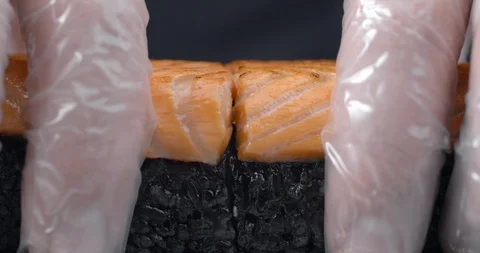 Chef splits in a half the sushi roll with black rice and salmon, cooking the raw Stock Footage 116444024