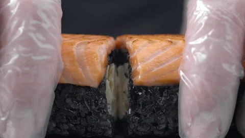 Chef splits in a half the sushi roll with black rice and salmon Stock Footage 143779644