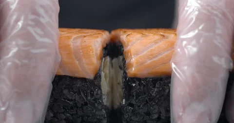 Chef splits in a half the sushi roll with black rice and salmon Video stock 143779662