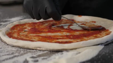 The chef spooning tomato sauce onto the raw pizza dough in the pizzeria. Stock Footage 344038355