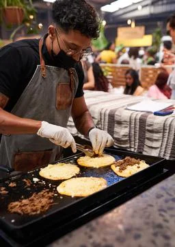 A chef spoons pulled beef onto tacos on the grill at a busy food market Stock Photos