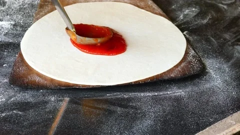 Chef spreading and applying tomato sauce on pizza on black background Stock Footage 221738048