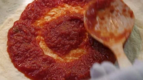 Chef spreading fresh tomato sauce on raw pizza dough with a ladle, close-up of a Stock Footage 337676877