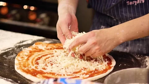 Chef spreading grated mozzarella cheese on pizza dough with tomato sauce in.. Stock Footage 334102191