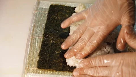 Chef spreads cooked rice by hand over a nori sheet for sushi preparation Stock Footage 346714819