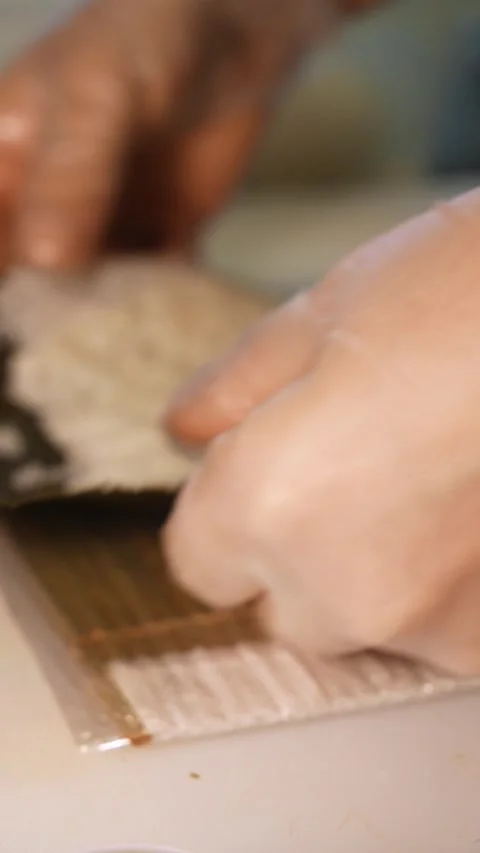 Chef spreads cooked rice by hand over a nori sheet for sushi preparation Stock Footage 346718039