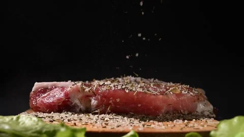 A chef sprinkles a blend of herbs over a raw steak placed on a wooden board. Stockbeeldmateriaal 305566484