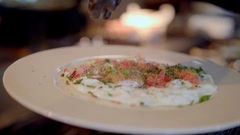 Chef sprinkles fresh herbs on fried eggs Stock Footage 99577199