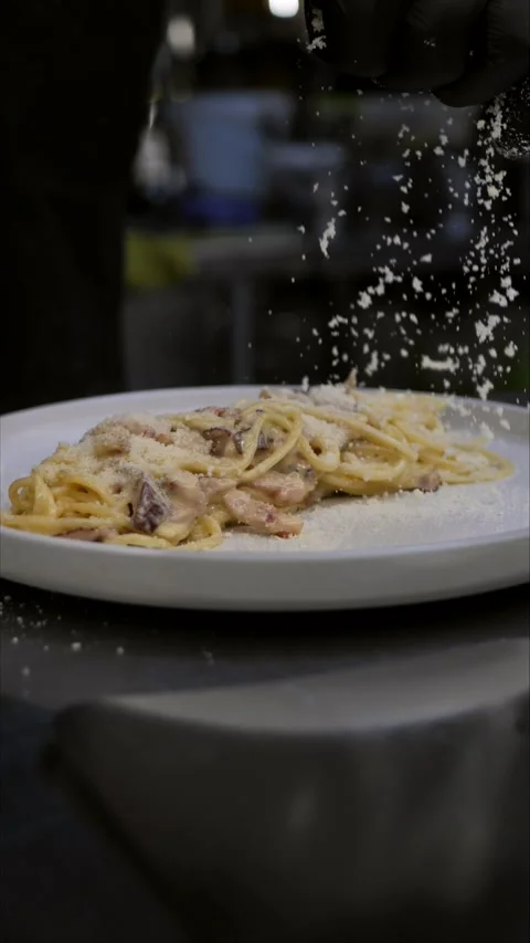 Chef sprinkles freshly cooked pasta with grated parmesan and pours green sauce Stock Footage 306846006