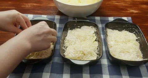 Chef sprinkles grated parmesan cheese over thinly sliced potatoes arranged in Vídeos de archivo 327628503
