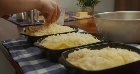 Chef sprinkles grated parmesan cheese over thinly sliced potatoes arranged in Vídeos de archivo 329520062