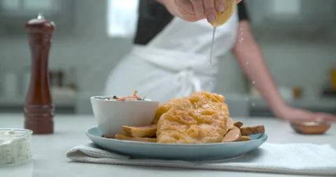 A chef squeezes a half cut lemon over a plate of gourmet battered fish and chips Stock Footage 199460522