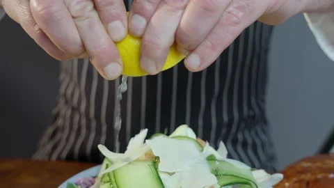 Chef squeezes a half cut lemon over a bowl of gourmet green salad. Stock Footage 234859771